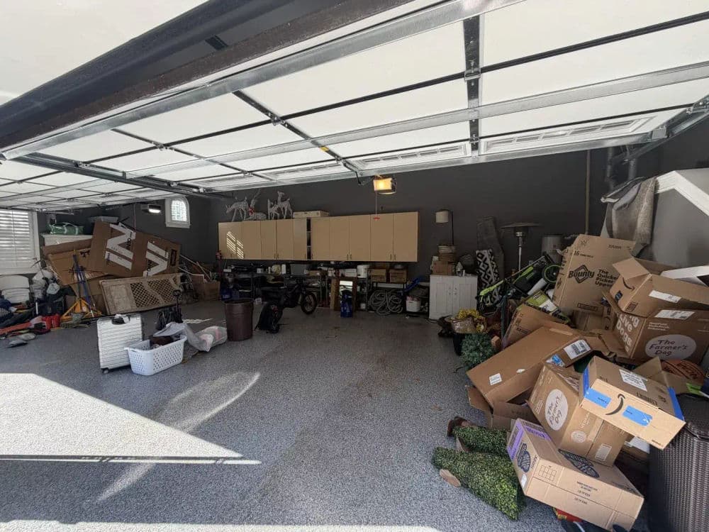 Cluttered garage filled with boxes, bikes, and storage items in disarray.